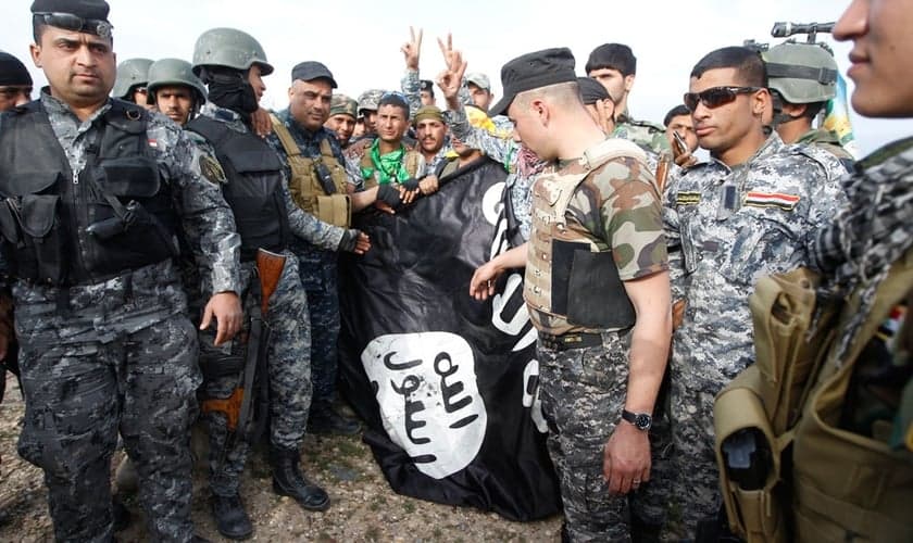 Homens da polícia iraquiana e combatentes xiitas seguram uma bandeira Estado Islâmico.