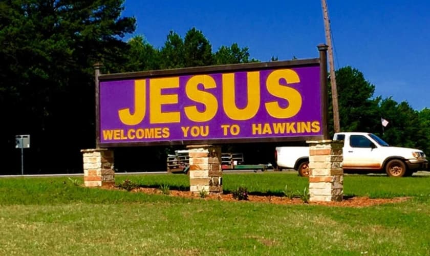 Em tradução, na placa está inscrita a frase "Jesus te dá boas-vindas à Hawkins".