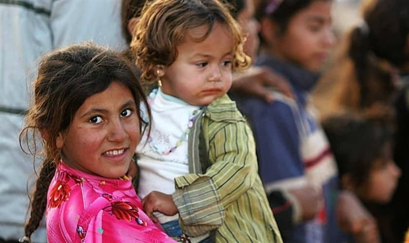Garota síria segura bebê no colo, em campo de refugiados. 