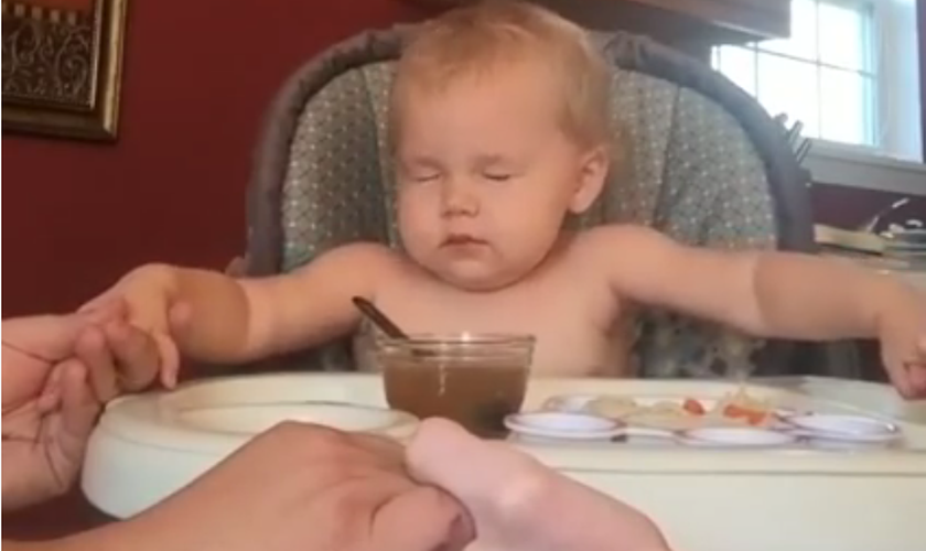 A pequena garotinha aperta as mãos de seus pais e fecha os olhos, preparada para um momento de agradecimento a Deus.  (Foto: Reprodução/ YouTube)