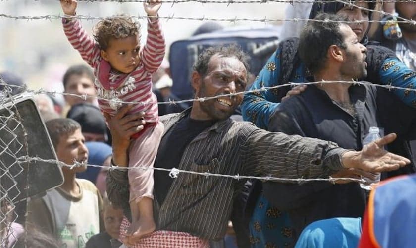 Refugiado sírio segura sua filha, enquanto tenta cruzar a fronteira da Turquia (Foto: Reuters)