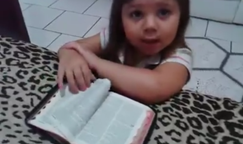 Ajoelhada em frente a uma cama, com os braços apoiados sobre uma Bíblia, a menina inicia suas preces. (Foto: Reprodução)