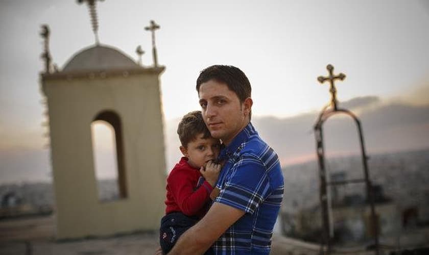 Homem cristão segurando seu filho, enquanto muitos de seus vizinhos fugiram da violência no Iraque. (Foto: Warrick Page/New York Times)