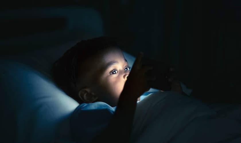 Imagem ilustrativa de menino deitado na cama com o celular. (Foto: iStock/Getty Images)