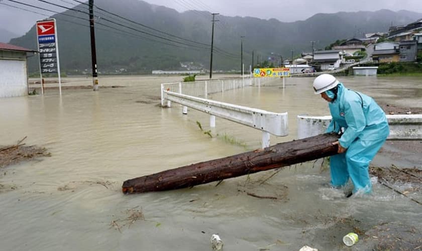 Japonês retira pedaço de árvore de Estrada inundada em Shingu neste sábado (10)