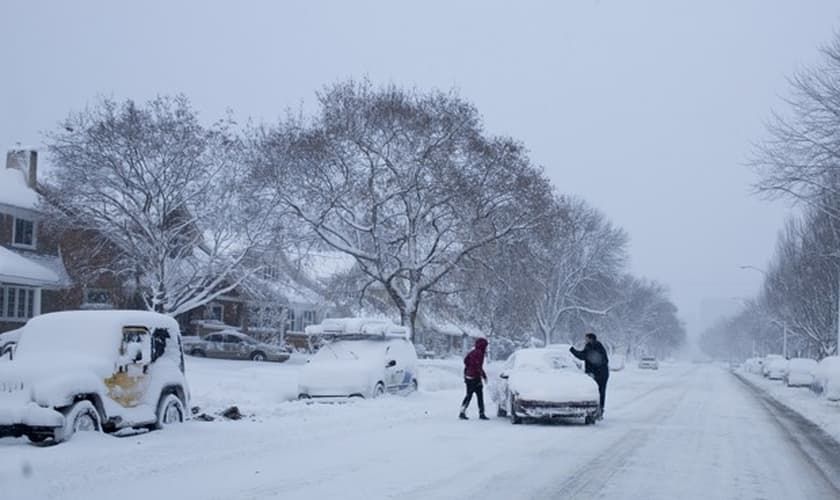 Pessoas tentam tirar veículo do meio de estrada em Lake Michigan Drive, no Michigan, na terça-feira (18) (Foto: AP Photo/The Grand Rapids Press, Joel Bissell )