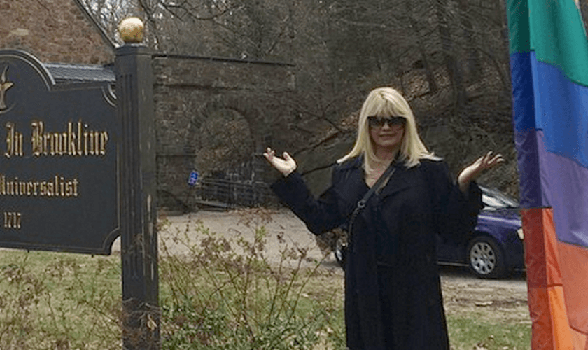 Monique Evans em frente a uma igreja, nos Estados Unidos, ao lado da bandeira LGBT.