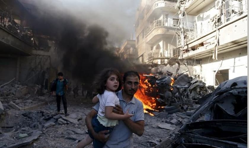 Homem leva uma garota nos braços, enquanto foge de um local atingido por ativistas, no bairro de Douma de Damasco (Síria), em agosto de 2015. (Foto: REUTERS/BASSAM KHABIEH)