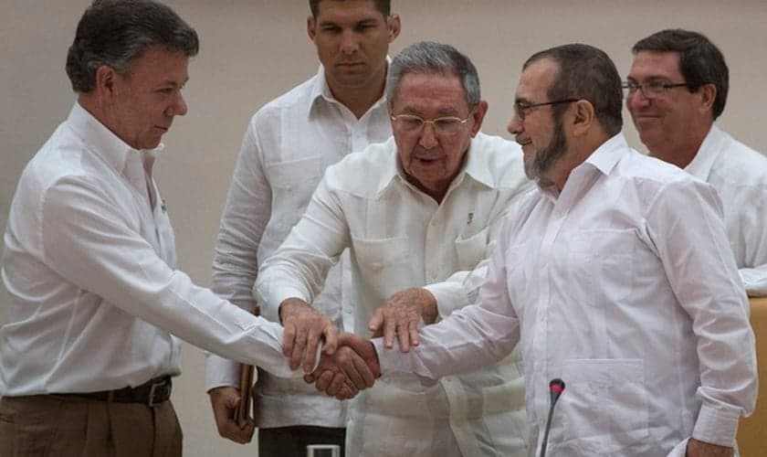 Presidente da Colômbia Juan Manuel Santos e o líder das FARC Timoleón Jiménez cumprem ato simbólico para acordo de paz, na frente do presidente cubano Raúl Castro (Foto: AP Photo / Desmond Boylan)