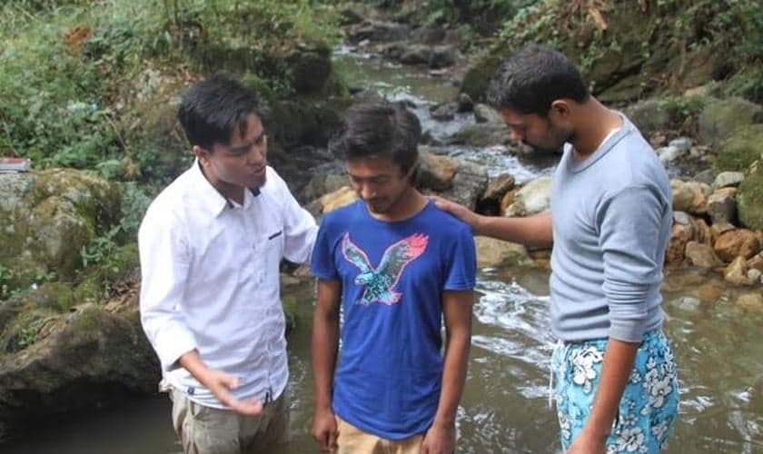 Pastor Lazrus e outro membro de sua equipe oram com jovem, antes de seu batismo, realizado em uma pequena cachoeira da região. (Foto: Levitas Nepal)