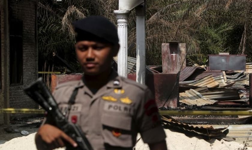 Policial segura rifle enquanto fica de guarda em frente a uma igreja queimada em Suka Makmur Village, em Aceh, Indonésia