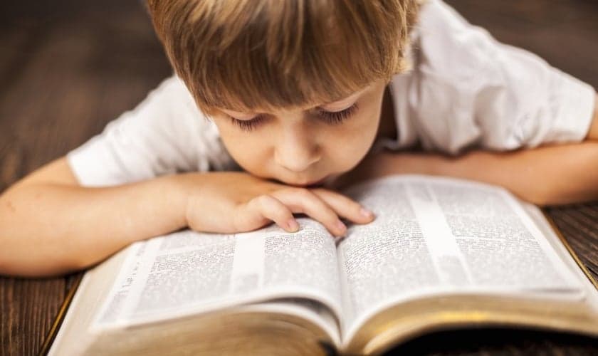 Garoto se debruça sobre Bíblia aberta. (Foto: Aim Lower Journal)