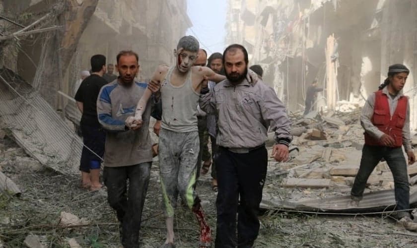 Sírios ajudam um jovem ferido após um ataque aéreo em Aleppo. (Foto: Ameer Alhalbi/AFP)