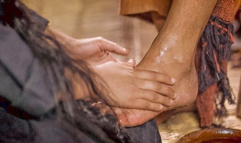 Maria derrama um caro perfume sobre os pés de Jesus, para depois enxugá-los com seus cabelos. (Imagem: Youtube)