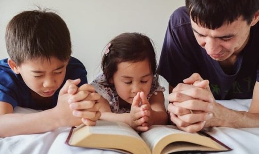 Pai lê a Bíblia com filhos. (Foto: Getty)