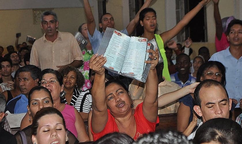Cristãos participam de culto em Cuba, enquanto uma das fiéis expõe sua Bíblia. (Foto: United Bible Societies)