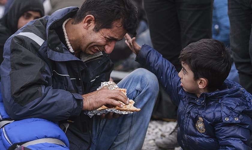 Garoto vê seu pai chorando durante um protesto de migrantes iraquianos do Paquistão e Marrocos. (Foto: CNS/Georgi Licovski/EPA)