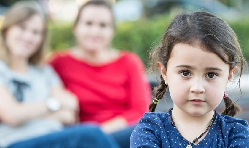 Imagem ilustrativa de criança com lésbicas ao fundo. (Foto: Considering Adoption)