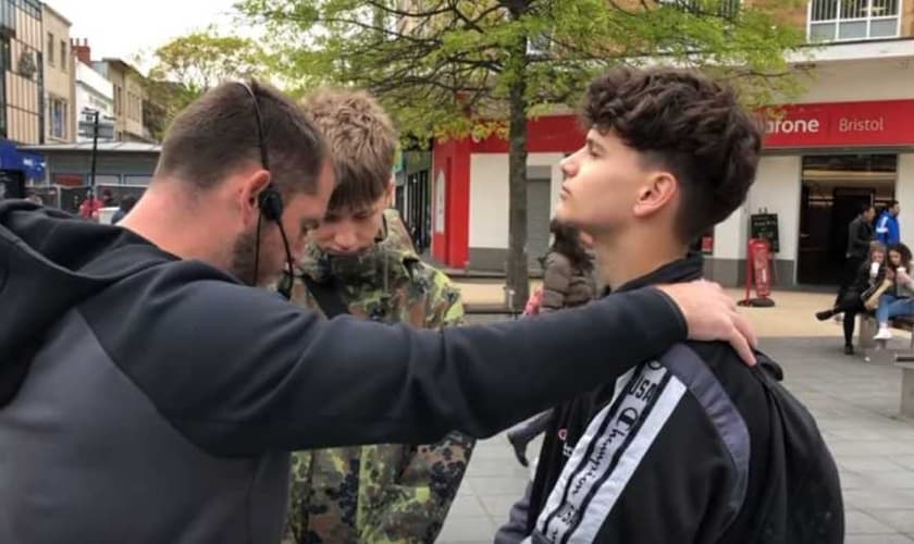 Evangelista Phillip Blair (esquerda) ora com os adolescentes Joe e Mathias, após pregar nas ruas de Bristol (Inglaterra) e fazer um apelo, perguntando quem gostaria de se entregar a Jesus. (Imagem: Youtube / Reprodução)