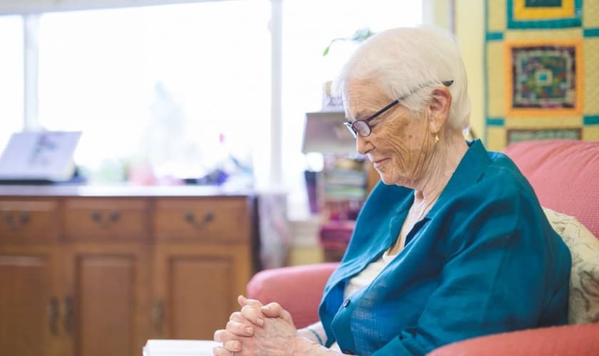 Mulher idosa orando enquanto lê a Bíblia em seu quarto. (Foto: FatCamera/Getty Images)