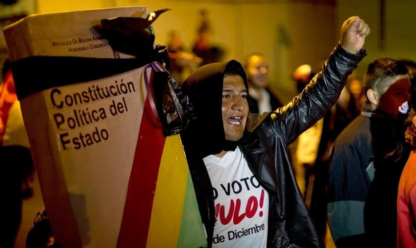 Manifestante com uma réplica gigante da constituição da Bolívia, embrulhada com uma fita preta de luto, em La Paz, Bolívia, em 2017. (Foto: Juan Karita/AP)