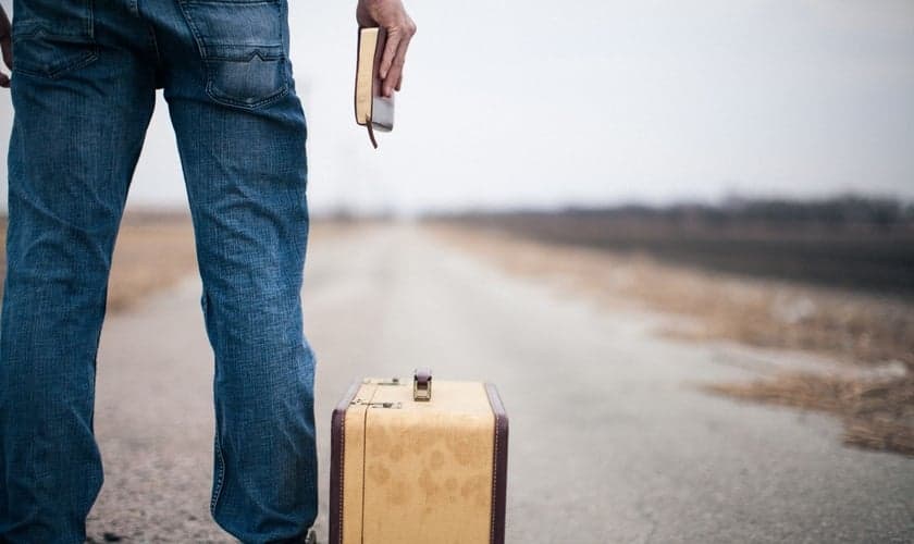 Imagem ilustrativa. Jovem segurando a Bíblia ao lado de uma mala. (Foto: Lightstock)
