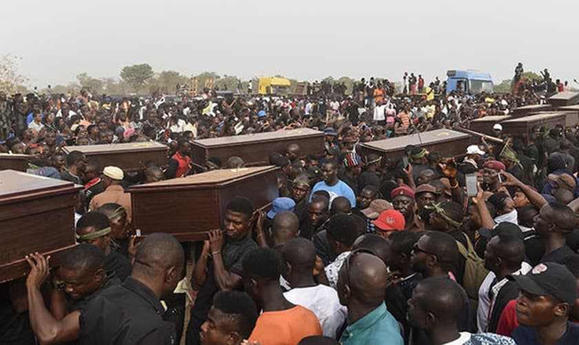 Homens carregam caixões em velório coletivo, após massacre na Nigéria. (Foto: Independent)
