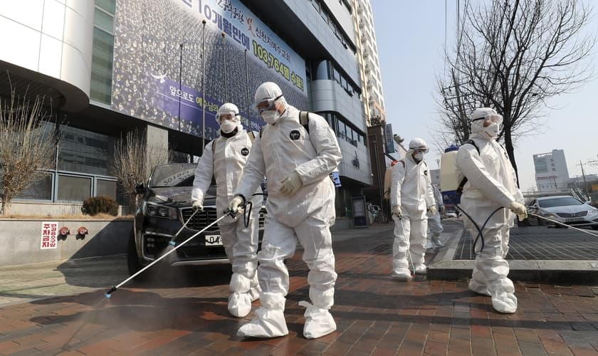 Trabalhadores com equipamento protetor usam desinfetante em spray contra o novo coronavírus em frente à igreja em Daegu, na Coreia do Sul, nesta quinta-feira (20). (Foto: Kim Jun-beom/Yonhap via AP)