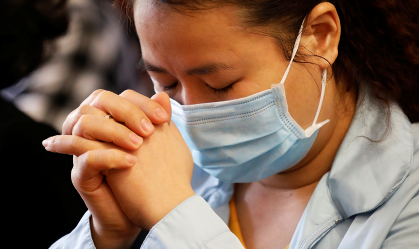 Uma mulher usa máscara enquanto ora em meio ao surto de coronavírus. (Foto do CNS / Kham, Reuters)