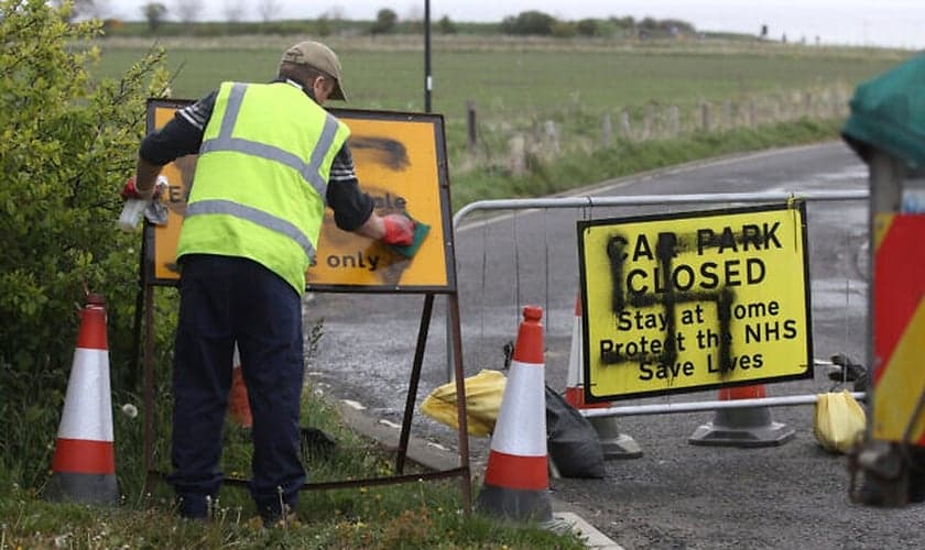 Trabalhador remove suástica pintada em uma placa na entrada de uma estrada fechada e parque de estacionamento perto do farol de Whitley Bay, em Northumberland, Inglaterra, quinta-feira, 30 de abril de 2020. (Foto: Owen Humphreys / AP)