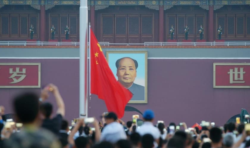 Visitantes acompanham uma cerimônia de hasteamento da bandeira com a imagem de Mao Tsé Tung ao fundo, na praça Praça da Paz Celestial, em Pequim, em julho de 2018. (Foto: CHINA STRINGER NETWORK/REUTERS/Newscom)