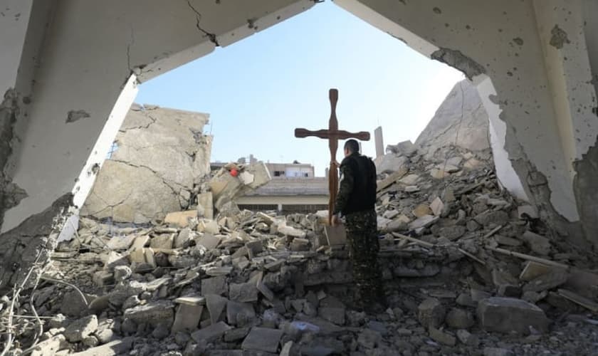 Um membro das forças árabes-curdas da Síria coloca uma cruz nos escombros antes de uma celebração de Natal na Igreja Católica Armênia dos Mártires, no centro da cidade de Raqa, leste da Síria, em 26 de dezembro de 2017. (Foto: DELIL SOULEIMAN / AFP)