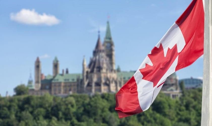 Bandeira canadense, com o parlamento ao fundo. (Foto: Reprodução / Shutterstock)