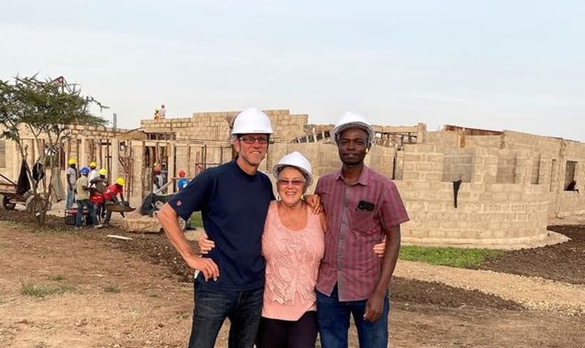 Darryl e Shirley Peters e auxiliar do casal, na Tanzânia; ao fundo, construção do centro de saúde. (Foto: Reprodução / CHVN Radio)