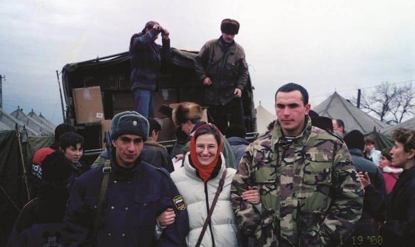 Paula O'Keefe entre soldados que protegem a distribuição de alimentos em um campo de refugiados chechenos. (Foto: Reprodução / Premier)