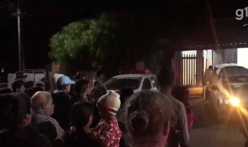 Enquanto os corpos eram retirados, os vizinhos oraram o Pai Nosso em frente a casa. (Foto: Reprodução/g1).