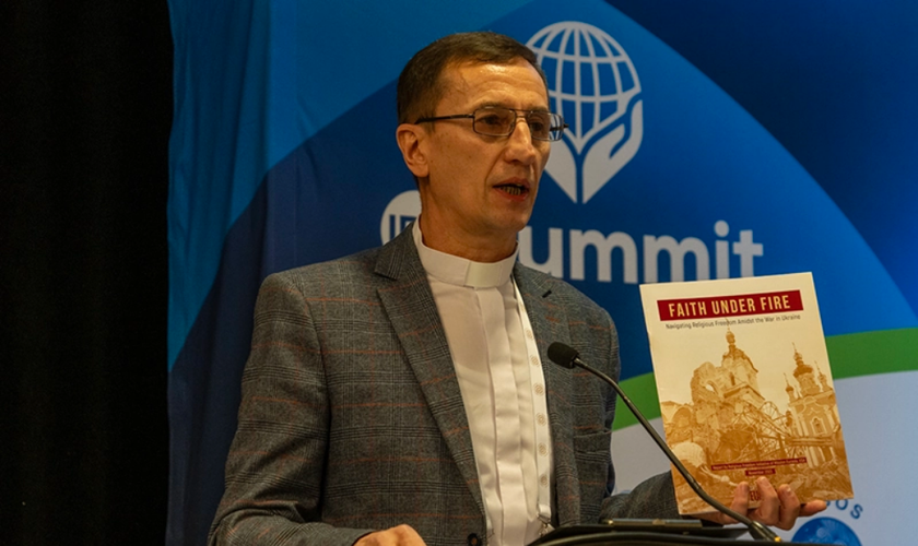 Pr. Mykhailo Brytsyn segurando o relatório “Fé sob Fogo” enquanto fala sobre sua experiência na guerra russa contra a Ucrânia. (Foto: Christian Daily International)